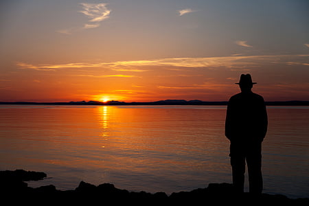 silhouette of man standing facing body of water thumbnail