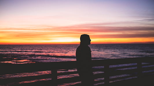 man leaning on fence near body of water thumbnail