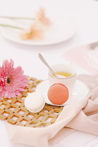 two french macarons near white ceramic coffee cup and pink petaled flower thumbnail