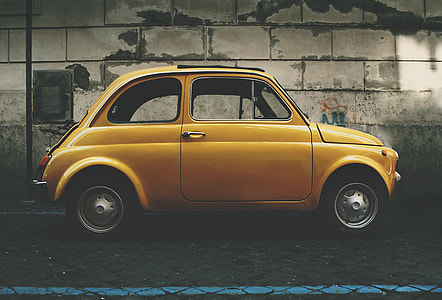 low light photography of yellow 3-door hatchback parked beside gray wall thumbnail