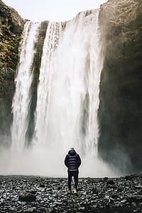man walking towards waterfall during daytime thumbnail