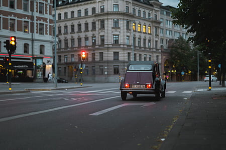 classic maroon car traveling on road near buildings at daytime thumbnail