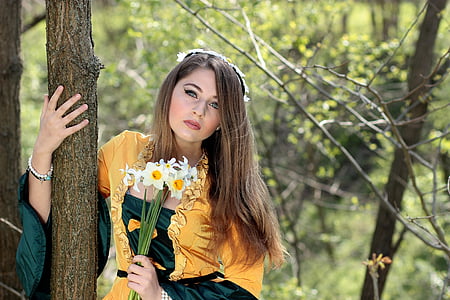 woman holding white petaled flowers standing beside brown tree trunk at daytime thumbnail