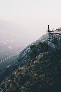 person standing on cliff with overlooking view of green fields at daytime thumbnail