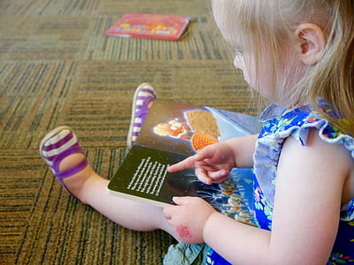 girl rearing book while sitting on brown floor thumbnail