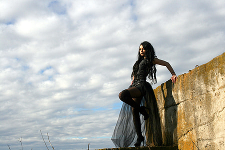woman wearing black gown standing beside concrete wall under cloudy sky during daytime thumbnail