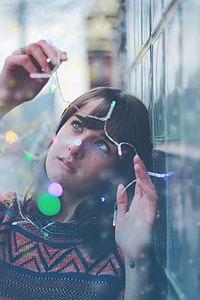 woman wearing orange and black crew-neck shirt holding string lights selective focus photography thumbnail