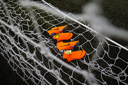 two pairs of orange Nike cleats on white soccer net thumbnail