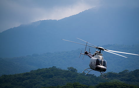 white helicopter flying above forest thumbnail