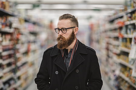 man with undercut hairstyle and beard wearing black eyeglasses in the middle of grocery isles thumbnail
