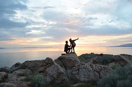 silhouette of man and woman on top of rock formation thumbnail