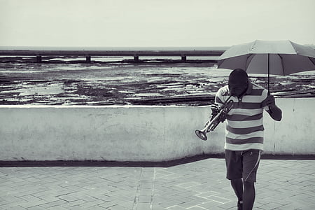 man playing trumpet while holding umbrella thumbnail