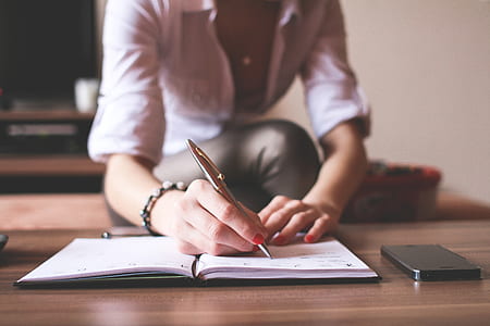 woman wearing white dress shirt writing on book with brown click pen thumbnail