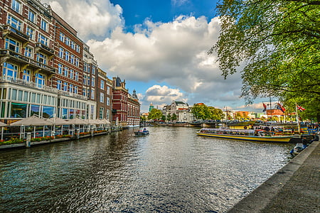 concrete buildings by the river and boats under white clouds and blue sky during daytime thumbnail