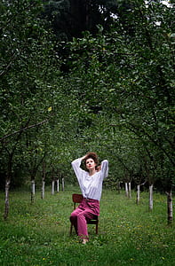 woman sitting on brown chair surrounded with trees thumbnail