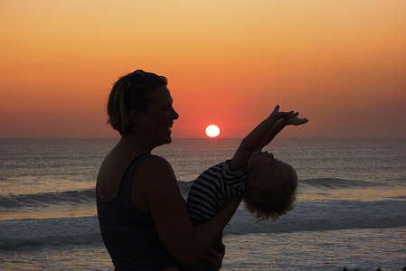 woman carrying her child near body of water during sunset thumbnail