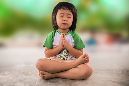 girl wearing white and green shirt sitting while praying on grey concrete floor thumbnail