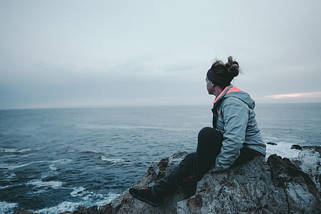 man sitting on rock near ocean thumbnail
