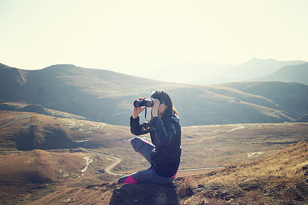 woman using binoculars sitting on ground during daytime thumbnail