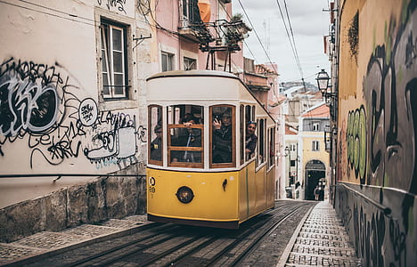 yellow and white tram train near white and brown concrete buildings thumbnail