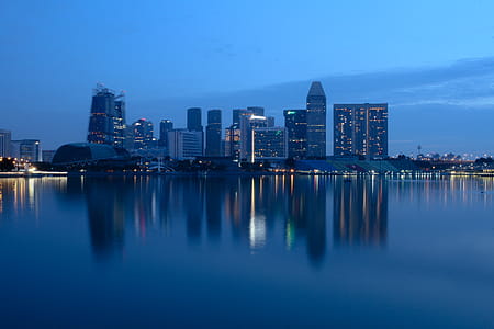 City Buildings Beside Body Of Water During Night Time thumbnail