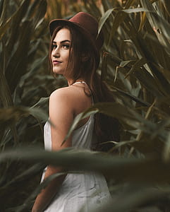 woman in white sleeveless dress standing surrounded by plants thumbnail