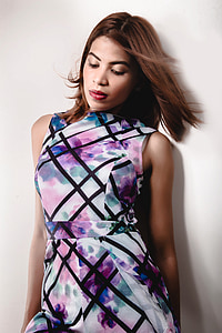 woman wearing white, purple, and black floral sleeveless dress leaning against white wall thumbnail
