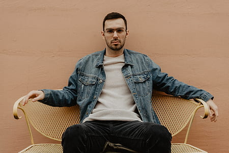 man wearing blue chambray jacket sitting on yellow metal bench thumbnail