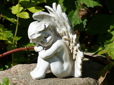 cherub on gray rock formation near green plants thumbnail