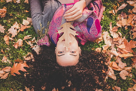Woman Lying Down On Green Grass Field Holding Brown Leaf thumbnail
