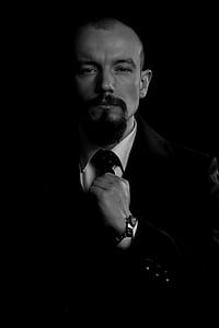 man in suit jacket holding his necktie in grayscale photography thumbnail