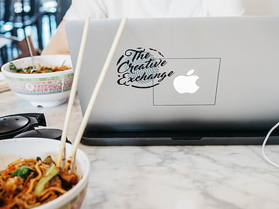 person using MacBook beside bowl of noodles on white marble table thumbnail