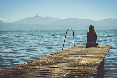 woman in black top sitting on brown wooden dock under blue sky during daytime thumbnail