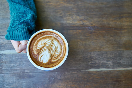 person in blue sweater holding cup of cappuccino thumbnail