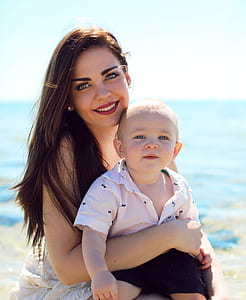 smiling woman carrying baby boy near body of water during daytime thumbnail