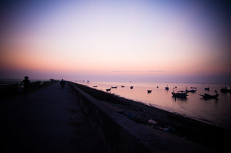 people on road near boats on ocean during sunset thumbnail