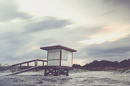 white and brown wooden lifeguard watch base on grey sand under grey sky thumbnail