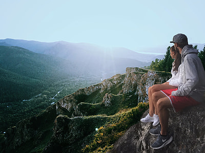 man and woman sitting on cliff overlooking sun rise over the hills thumbnail