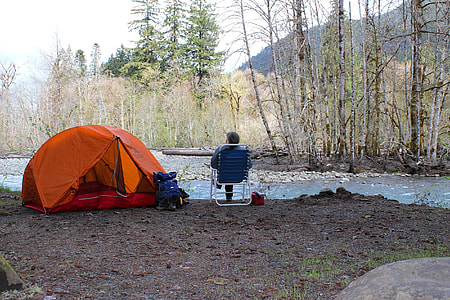 man sitting on folding armchair beside orange tent thumbnail