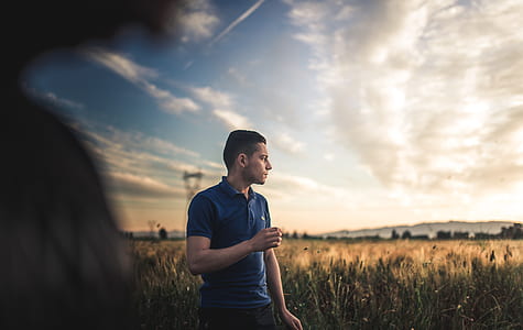 man wearing blue polo shirt standing on green grass looking onto golden hour thumbnail
