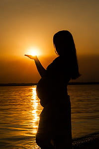 silhouette photography of pregnant woman standing on sea shore thumbnail
