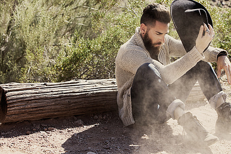 man holding hat sitting near wood trunk during daytime thumbnail