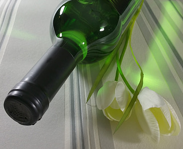 green glass bottle beside two white tulip flowers thumbnail