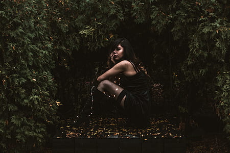 woman sitting surrounded by green leaf plants thumbnail