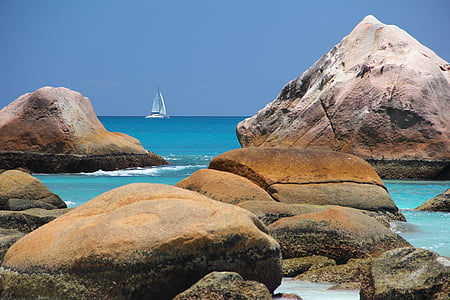 brown and gray rocks in seashore with white boat in the background thumbnail