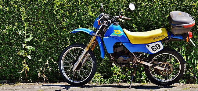 blue and yellow motocross dirt bike beside bush thumbnail