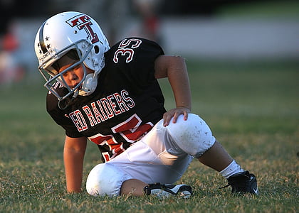 boy wearing football gear sitting on grass thumbnail