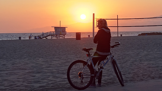 man sitting on bicycle facing sea under orange sky thumbnail