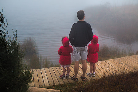 man in black jacket with two children in red jackets facing a lake thumbnail