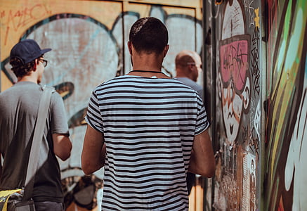 three men standing beside graffiti wall during daytime thumbnail